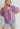 Model wearing the Nimes Top — lilac short-sleeve blouse with square neckline, puff sleeves, and textured stitching, styled with denim shorts for a soft bohemian look.