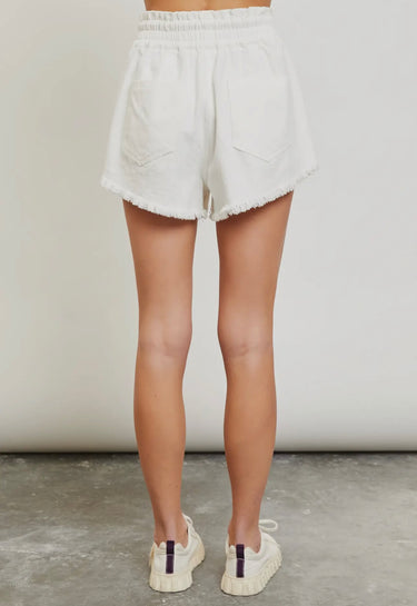 Model wearing white frayed short  with drawstring waist and sneakers — casual summer look, back view
