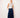 Woman wearing a white sleeveless top and blue wide-leg jeans against a plain background