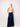 Woman wearing a white sleeveless top and blue wide-leg jeans against a plain background