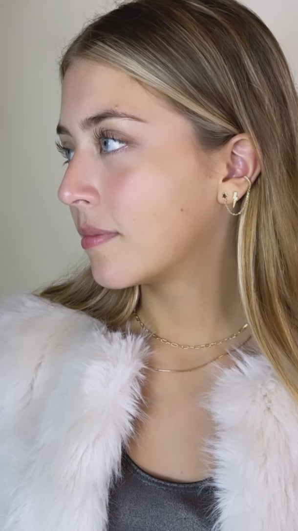 Model wearing Sherpa stud earrings in gold with layered necklaces on beige background
