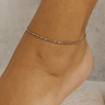 Close-up of a foot wearing a delicate silver anklet on a neutral background