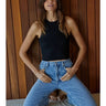 Model wearing the black Romett Top with a ribbed knit texture, mock neckline, sleeveless cut, fitted cropped silhouette, and relaxed light-wash denim jeans.