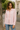 woman wearing Rosewood Ruffle Blouse in light pink, long sleeves, button-down with ruffle trim, styled with blue jeans on the street