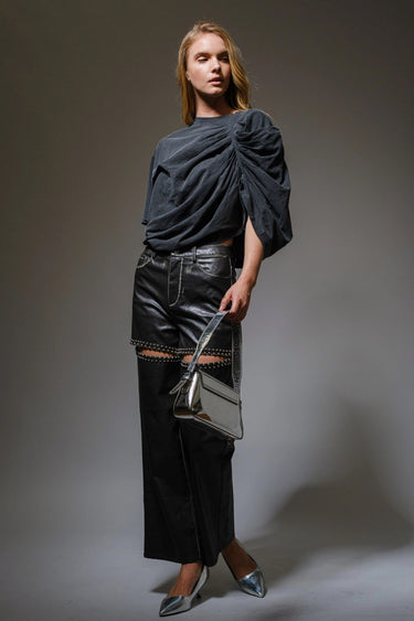 Woman wearing the Roux Top in charcoal black with sculpted ruching and dramatic draped detail, styled in soft natural light on a neutral background.