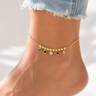 Model wearing Syrath Anklet gold anklet with multicolor crystal charms and dangling bead details.