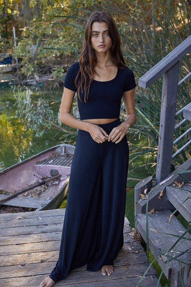 Full-body view of the Tamara Top in black paired with a flowing black maxi skirt, showcasing the fitted ribbed crop top, scoop neckline, and versatile everyday styling.