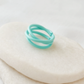 Turquoise adjustable ring with intertwined bands displayed on a beige stone background – Celeste Adjustable Ring by Matte