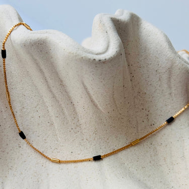 Unify Necklace by Matte, gold plated chain with black beads on cream textured surface