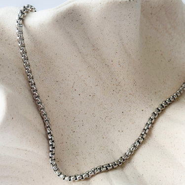 Silver chain necklace on a textured beige surface