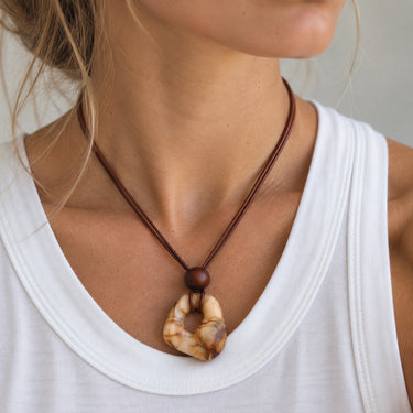 Vina Necklace by Matte styled on a model, featuring a long brown cord and sculptural marbled amber and cream pendant for an earthy statement look.