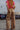 Person wearing a pink top and leopard print pants standing in an outdoor setting with cars in the background.