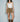 Woman wearing the Yagu Skirt, a suede-look western-inspired mini skirt featuring silver stud detailing, adjustable side buckle, high-rise waist, and rich camel color styled with a white tank top and cowboy boots.